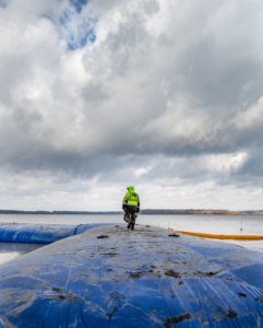 A worker on a blue water barrier during a shoreline construction project by Wilkinson Excavating, Inc. in Meadville, PA