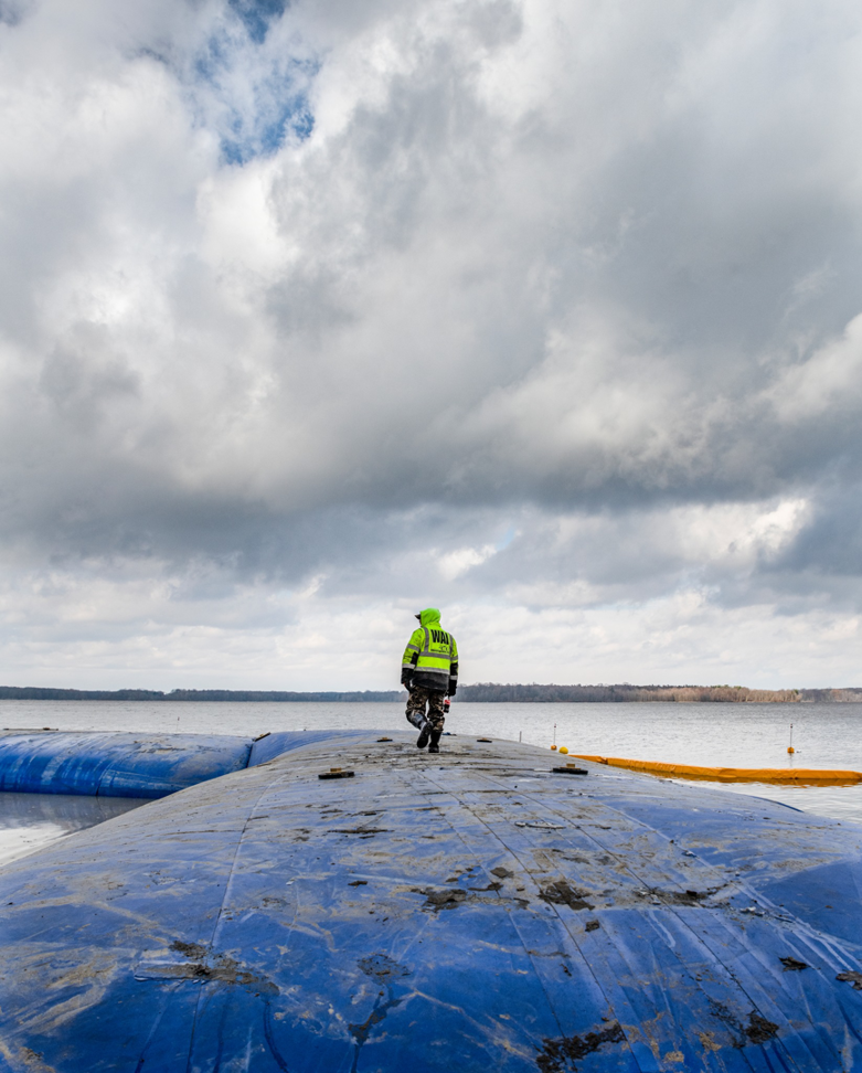 A worker on a blue water barrier during a shoreline construction project by Wilkinson Excavating, Inc. in Meadville, PA