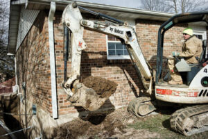 A Helitech Waterproofing & Foundation Repair worker operating an excavator for foundation repair in Kingdom City, MO.