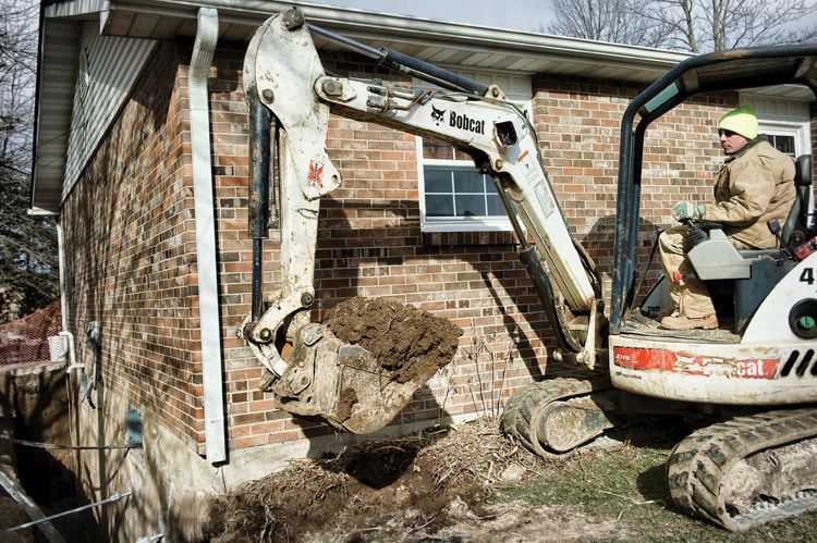 A Helitech Waterproofing & Foundation Repair worker operating an excavator for foundation repair in Kingdom City, MO.