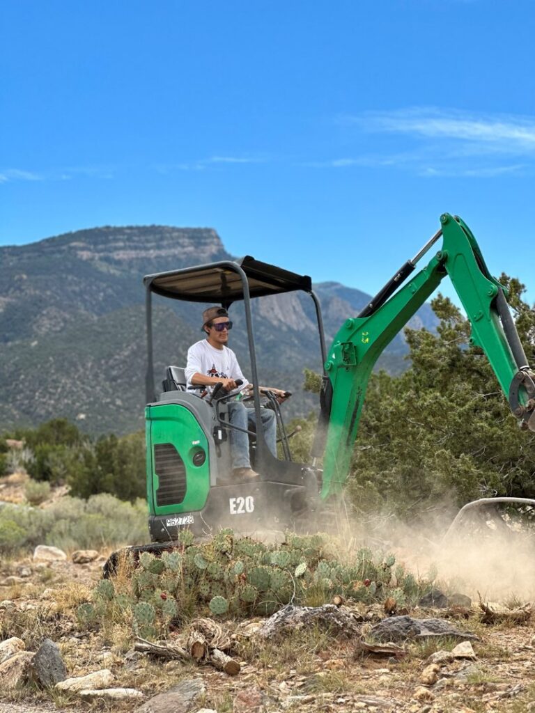 A worker operating a mini excavator for brush clearing services by Sandia Valley Services LLC in Rio Rancho, NM.