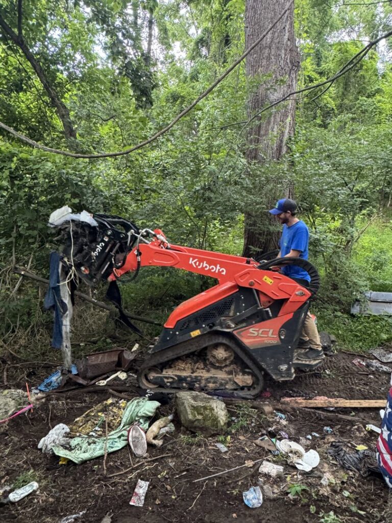 A worker from Barkers Junk Removal & Hauling LLC operating a Kubota skid steer to clear junk from an overgrown area in Roanoke, VA.