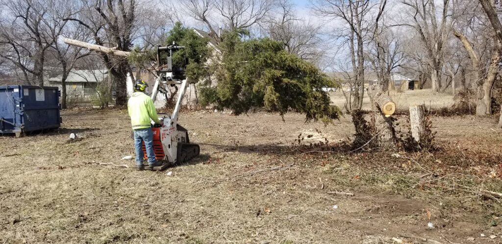 A worker from Arbor Med Tree Service operating a skid steer to move a large tree branch in Wichita, KS.