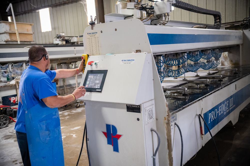 A worker operating a stone edge finishing machine for countertops at L&M Granite Countertops in Phoenix, AZ.