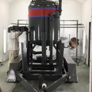 A worker painting a large industrial vessel inside a spray booth for Alpine Painting and Sandblasting Contractors in Paterson, NJ.