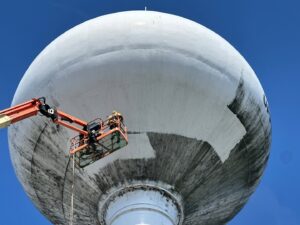 A worker in a boom lift painting a large water tower for Alpine Painting and Sandblasting Contractors in Paterson, NJ.