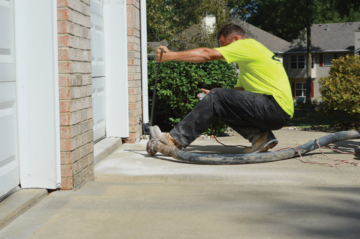 A Helitech Waterproofing & Foundation Repair worker performing concrete leveling on a driveway in Kingdom City, MO.