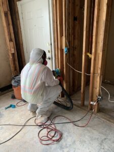 Worker in full protective gear performing remediation work in a room with exposed studs for Coyote Restoration in North Richland Hills, TX.