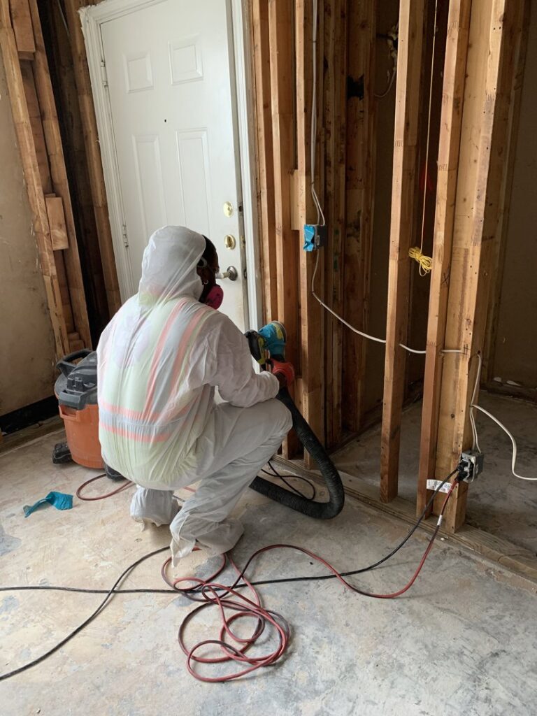 Worker in full protective gear performing remediation work in a room with exposed studs for Coyote Restoration in North Richland Hills, TX.