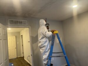 A worker in full protective gear spraying a ceiling during remediation work for Coyote Restoration in North Richland Hills, TX.