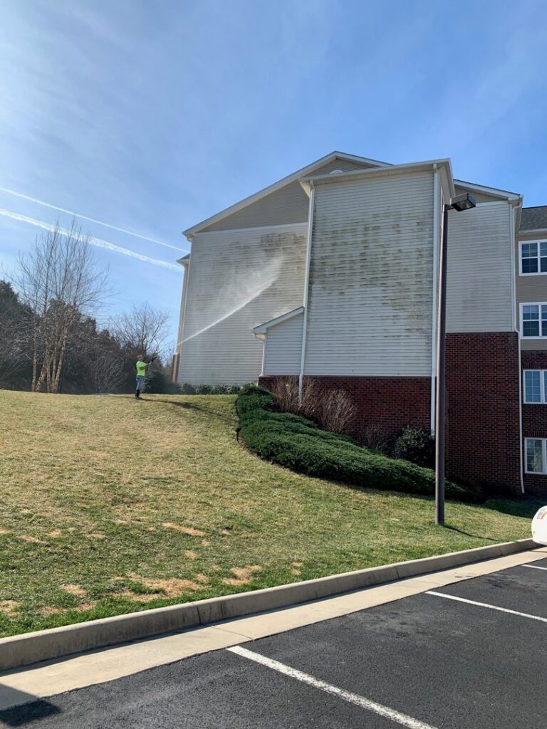 A worker professionally pressure washing the siding of a large building for On Time Performance in Richmond, VA.
