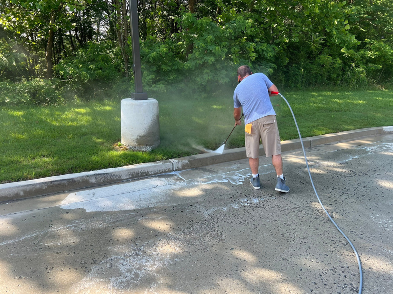 A worker pressure washing a concrete curb and asphalt parking lot for Selk Solutions in Crossville, TN.