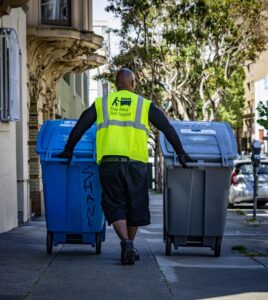 A Bay Area Bin Support worker pushing two residential waste bins along a sidewalk in San Leandro, CA.