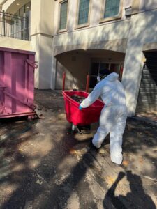 A worker in a protective suit pushing a cart of debris towards a dumpster for Professional Restoration in Jersey City, NJ