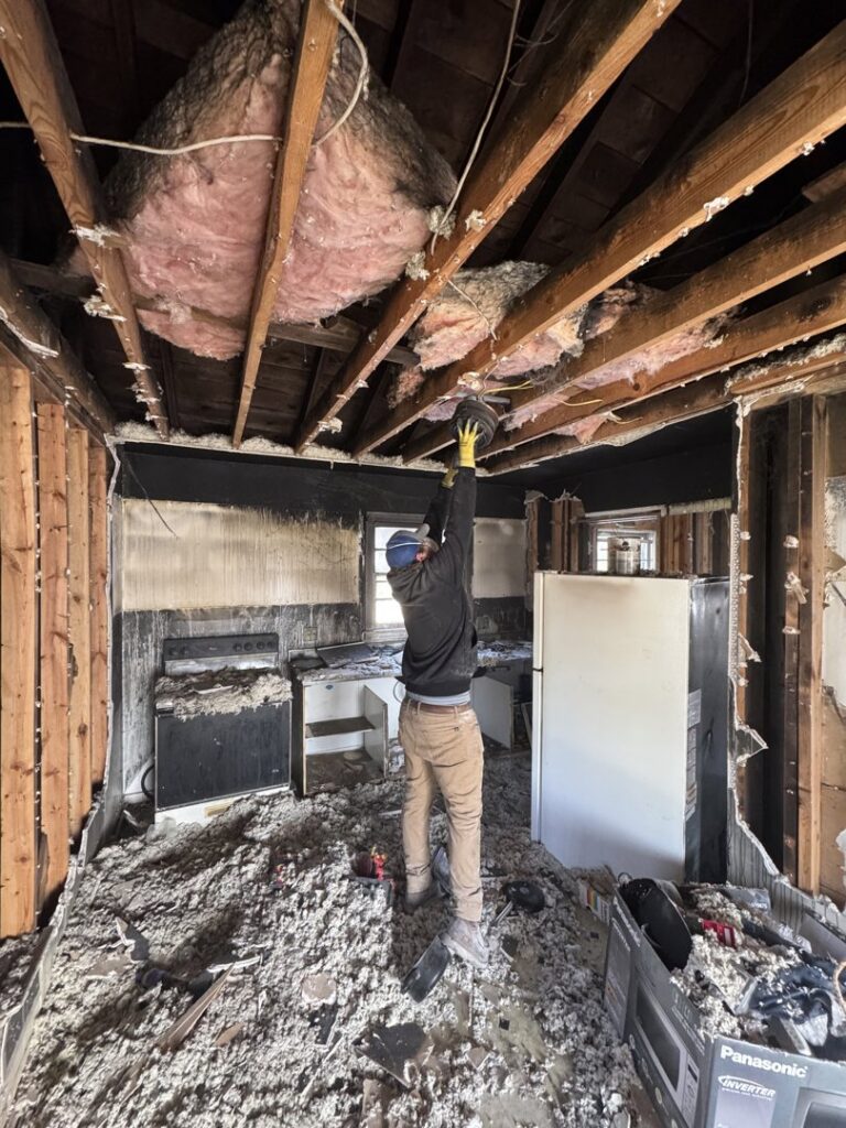A worker removing debris from the ceiling in a fire-damaged kitchen, demonstrating junk removal by Barkers Junk Removal & Hauling in Roanoke, VA.