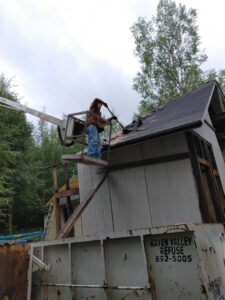 A worker on a lift removing roof debris into a Raven Valley Refuse and Recycling dumpster in Wasilla, AK.