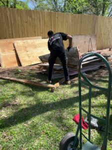 A NTX Haul Away Junk Removal worker clearing wood planks and construction debris from a backyard in Fort Worth, TX.