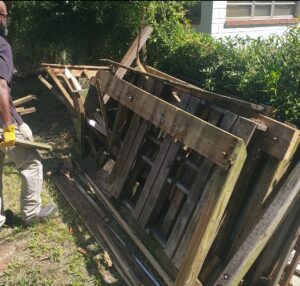 A worker in gloves removing wooden pallets and debris from a yard, demonstrating junk removal by Junk Fade Away, LLC in Jacksonville, FL.