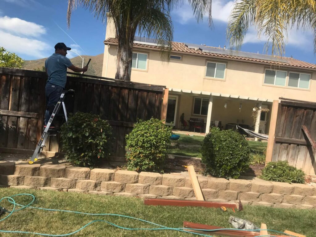 A worker on a ladder repairing a backyard wooden fence, demonstrating services by Juancho's Handyman in Salida, CO.