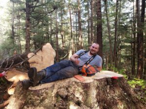 A worker resting on a large tree stump after completing tree removal work for Timberscape Industries LLC in Ketchikan, AK.