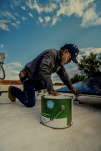 A worker performing roof repair near solar panels on a flat roof, a service by Campos & Son Roofing and Construction in El Paso, TX