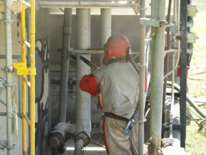 A worker in full protective gear sandblasting industrial pipes for WW Enroughty & Son, Inc. in Richmond, VA.