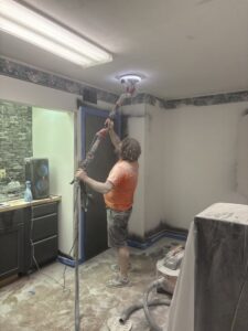 A worker using a long-handled sander to finish a ceiling, demonstrating drywall and painting prep by Byrd Property Restoration, LLC in Parkersburg, WV.