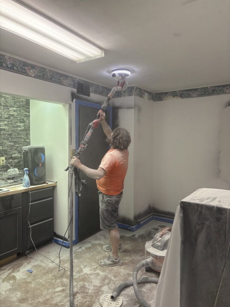 A worker using a long-handled sander to finish a ceiling, demonstrating drywall and painting prep by Byrd Property Restoration, LLC in Parkersburg, WV.
