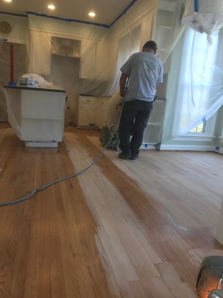 A handyman operating a floor sanding machine to refinish hardwood floors in a kitchen by Franco's Hardwood Flooring in Durham, NC.