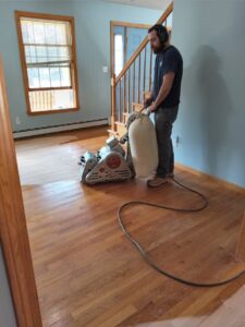 A worker operating a large floor sander to refinish a wood floor by Robert C. Mihaich Wood Flooring in Worcester, MA.
