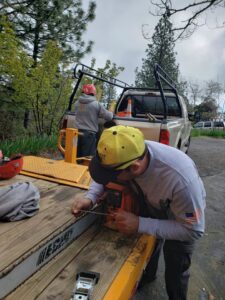 A Dry Leaf Tree Service LLC worker sharpening a chainsaw on a trailer, preparing for tree work in Sacramento, CA.