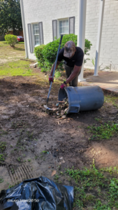 A worker shoveling debris and trash into a large bin during a clean-up job by Ashworth Clean Up Crew LLC in West Columbia, SC.