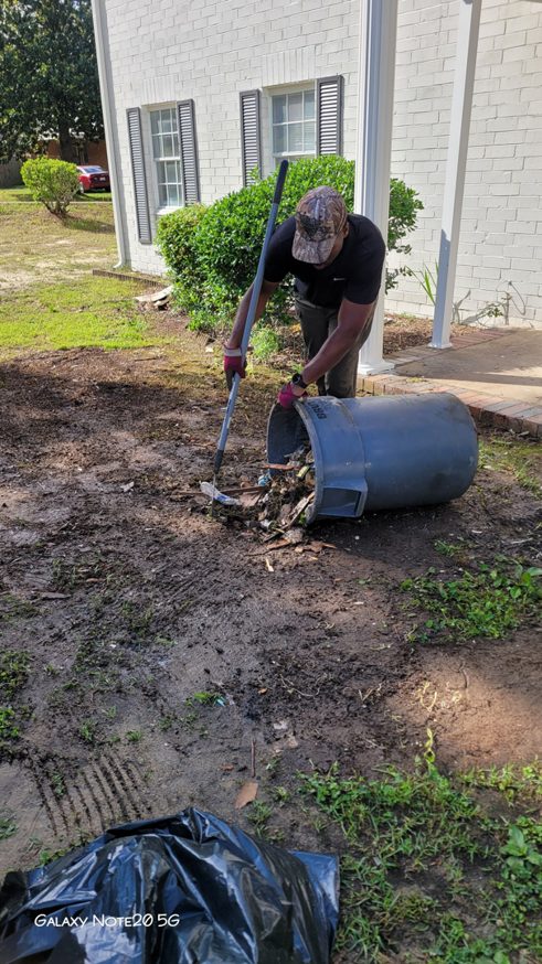 A worker shoveling debris and trash into a large bin during a clean-up job by Ashworth Clean Up Crew LLC in West Columbia, SC.