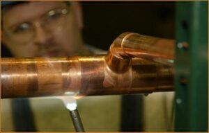 A skilled worker soldering copper pipes, demonstrating the detailed craftsmanship by McKamish, Inc. in Pittsburgh, PA