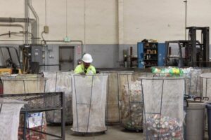 A worker sorting recycled materials like cans and bottles into large mesh bins at SA Recycling - Long Beach Ave in Los Angeles, CA.