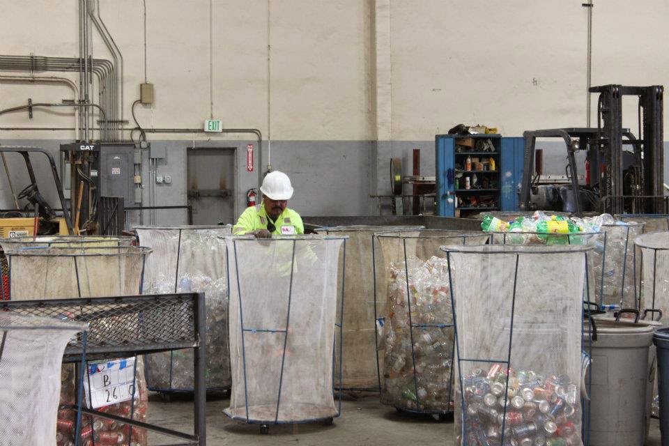 A worker sorting recycled materials like cans and bottles into large mesh bins at SA Recycling - Long Beach Ave in Los Angeles, CA.