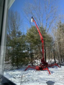 A Collins Tree Service, Inc. worker using a red spider lift for tree trimming in a snowy landscape in Hooksett, NH.