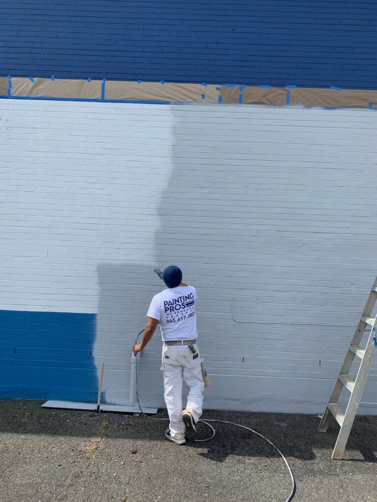 A worker spray painting an exterior brick wall, showcasing services from Painting Pros of Knoxville in Knoxville, TN.