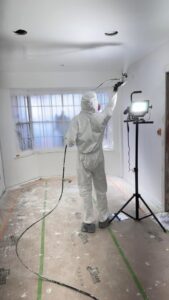 A worker in a protective suit spray painting a room during a remodel project by Forged Builds Custom Remodels in El Paso, TX.