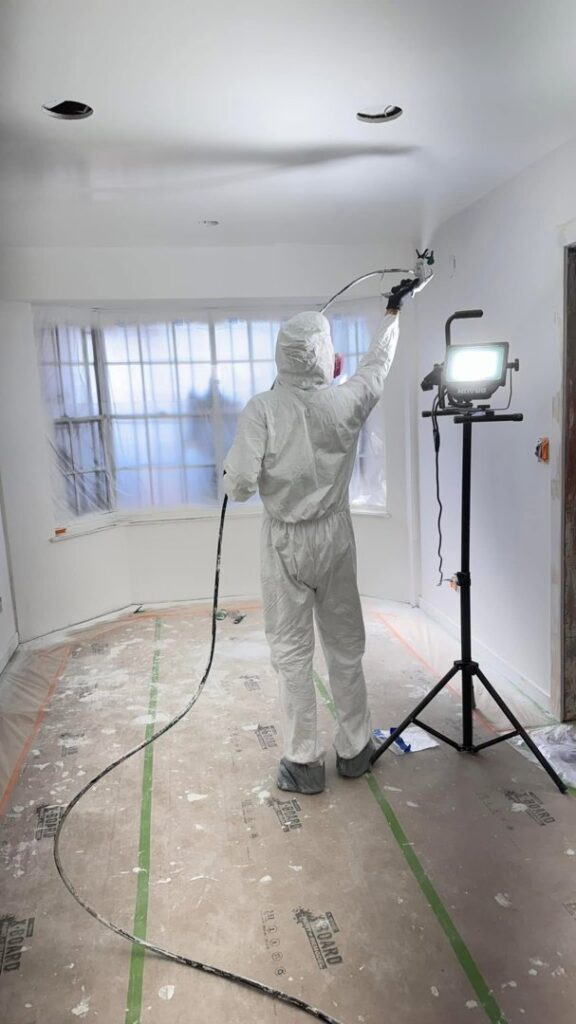 A worker in a protective suit spray painting a room during a remodel project by Forged Builds Custom Remodels in El Paso, TX.