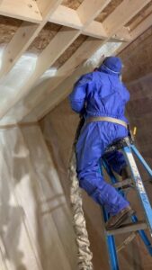 A worker in a protective suit spraying foam insulation onto an attic ceiling for Metro Insulation in Rockford, IL.