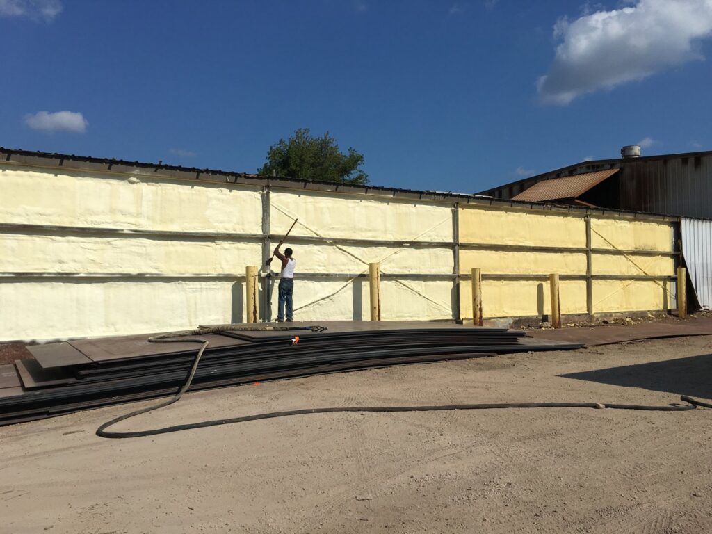 A worker spraying foam insulation onto the exterior wall of a commercial building for Metro Insulation in Rockford, IL.