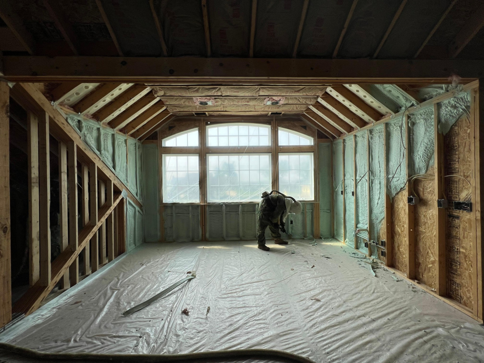 An Insulation Man professional applying spray foam insulation to a room with multiple windows in Chesterfield, MI.