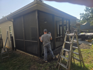 A worker applying stain to the exterior of a screened porch, part of a restoration service by CParks Pressure Washing and Deck Restoration in Columbia, MO.