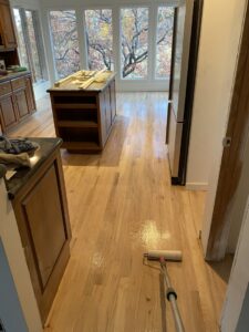 A worker staining or finishing stairs in a room with newly installed dark hardwood floors by IHS flooring LLC in Brighton, CO.