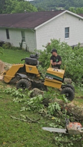 A worker operating a stump grinder with a chainsaw nearby, provided by Juarez Tree Service in Bawcomville, LA.