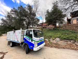 A worker sweeping debris into a Republic Junk Removal truck at a job site in San Diego, CA.