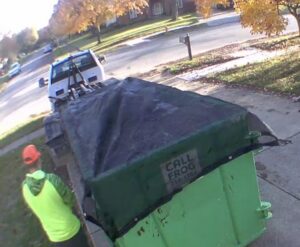 A worker tarping a full green Frog Hauling dumpster, preparing for pickup in Columbus, OH.