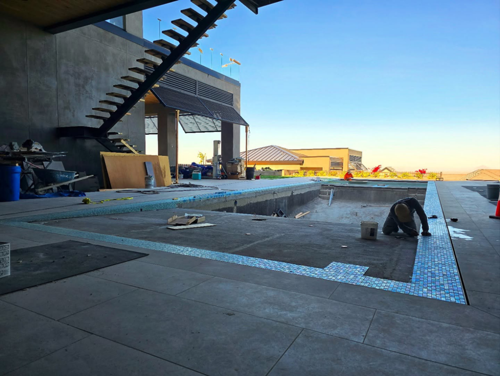 A worker carefully tiling the edge of a pool during construction by Premier Paradise, Inc. in Gilbert, AZ.