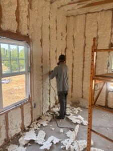 A worker trimming excess spray foam insulation from a wall after application by Off-Axis Spray Foam and Radon Services in Clarksville, TN.
